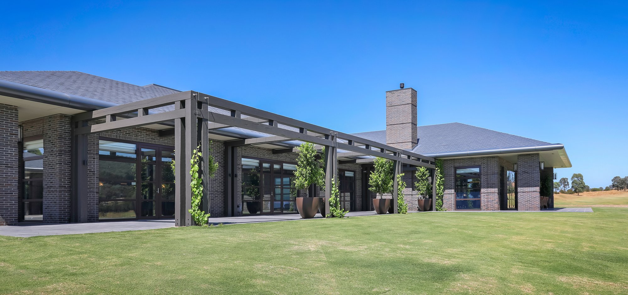 Eastern Golf Club Contemporary brick facade featuring a timber pergola, large glass doors, landscaped courtyard, and lawn.